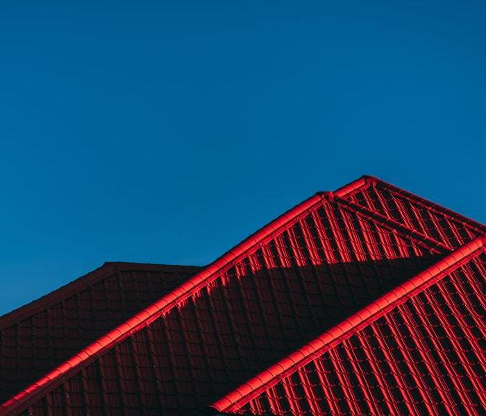 A red roof sits atop a building, with shingles of various shades of red. The roof is sharply angled and appears to be made of
